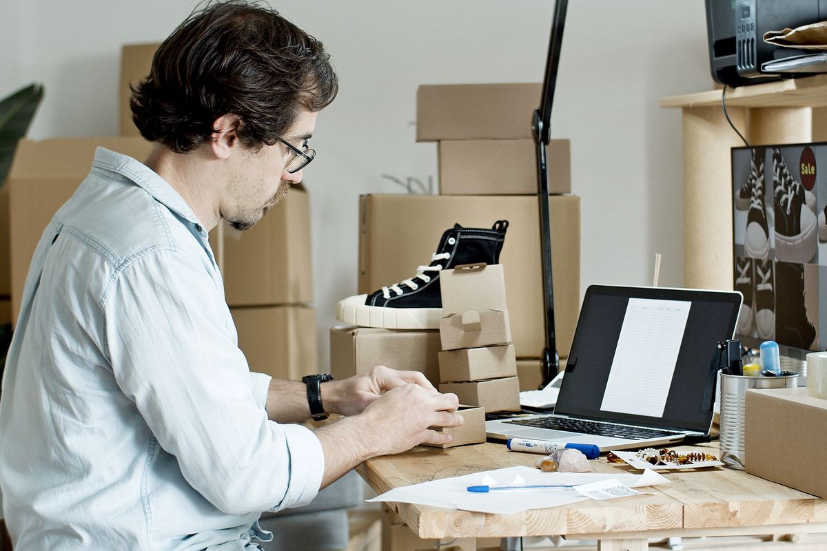Laptop bulunan çalışma masasında gönderilecek ürünleri paketleyen işletmeci.
